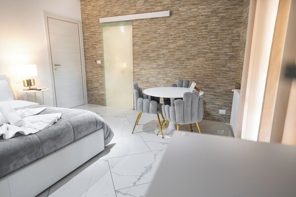 Una habitación de hotel moderna con una cama, una mesa redonda con sillas, una mesita auxiliar y una pared con textura similar a la madera.