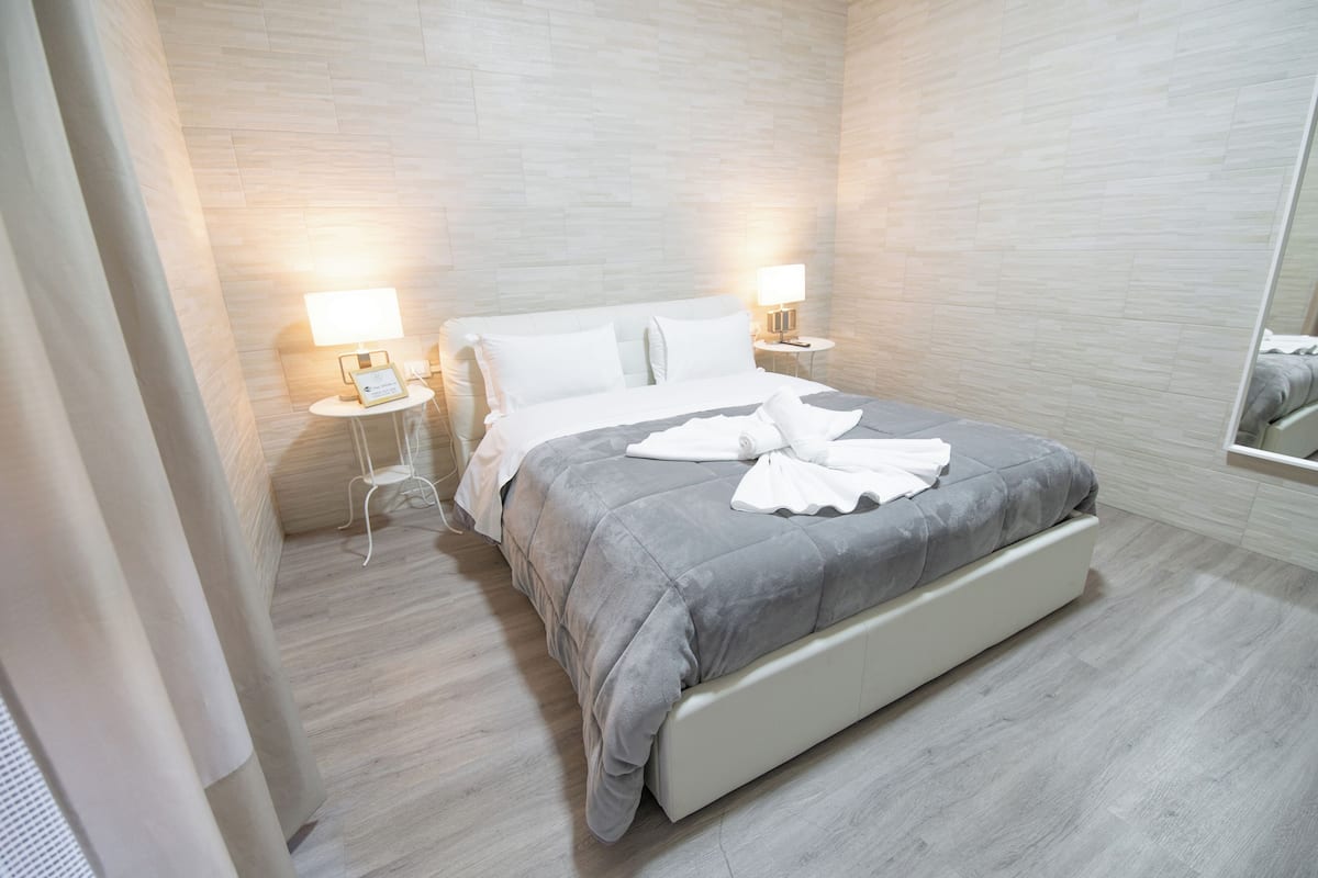 Moderni hotellihuone, jossa on suuri sänky, kaksi yöpöytävalaisinta ja peili seinällä.