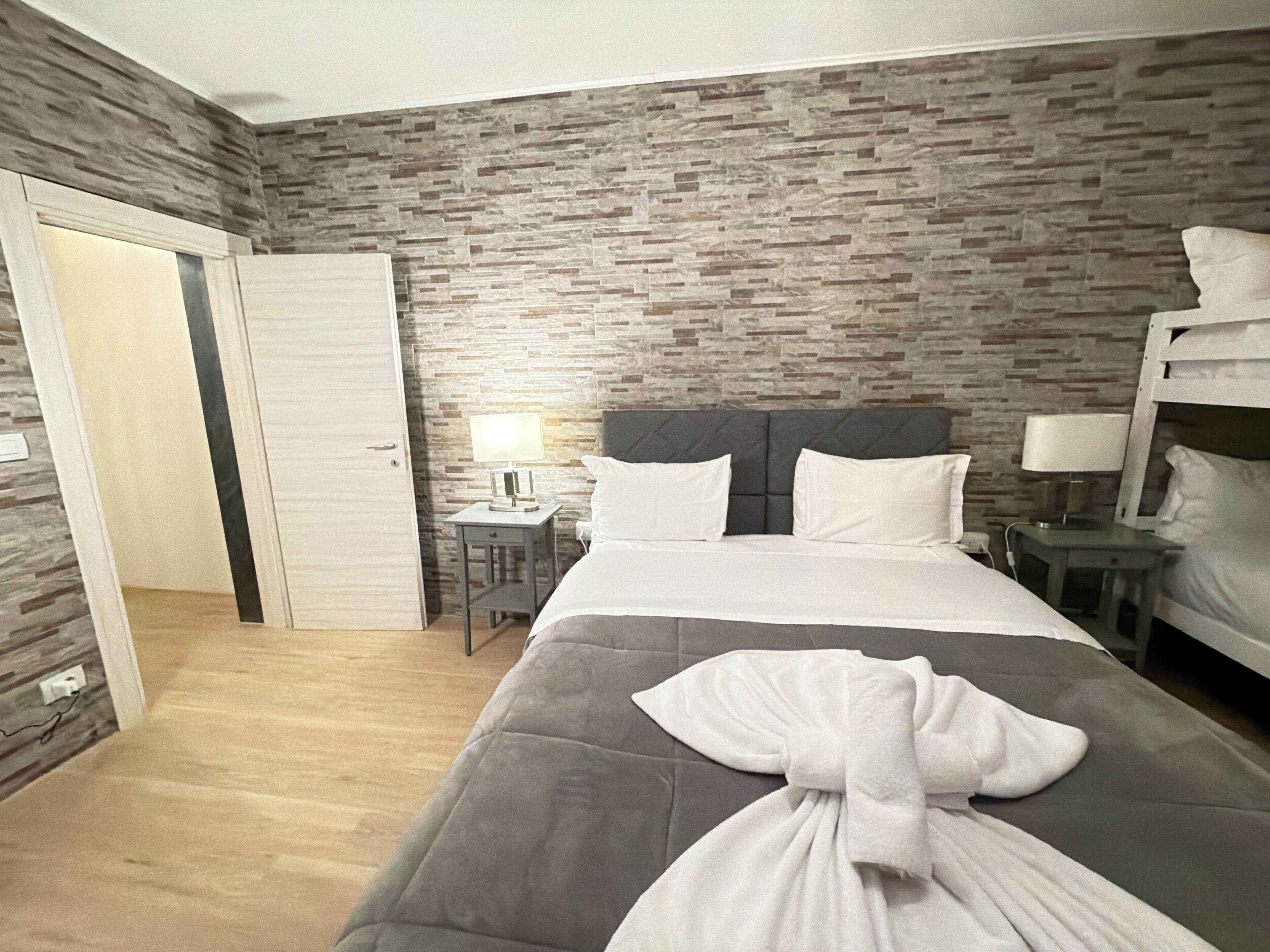 A hotel room with a bed, a nightstand, a lamp, a wardrobe, and a brick-patterned wall.