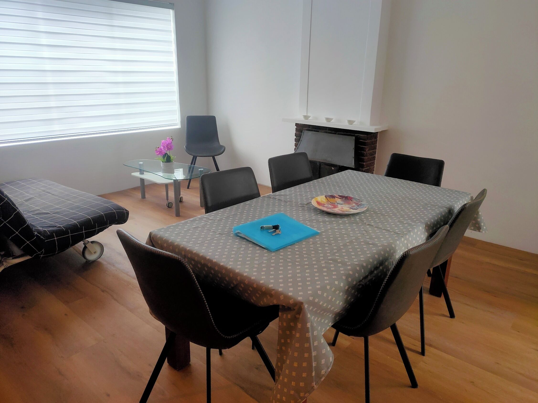 Un espace repas comprenant une table, des chaises, une petite table avec un plateau en verre et une chaise à roulettes.
