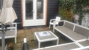 En terrasse med hvide udendørs møbler, herunder en sofa, stole, et lille bord og en parasol.
