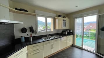 A modern kitchen with a large window, dark flooring, and light-colored cabinets.