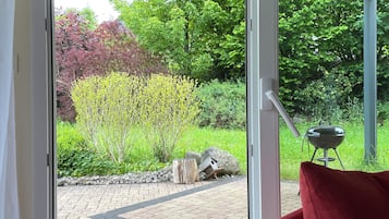 Een kamer met een schuifdeur naar een terras buiten, met een terrasvloer van baksteen, een houten stronk en een barbecue.
