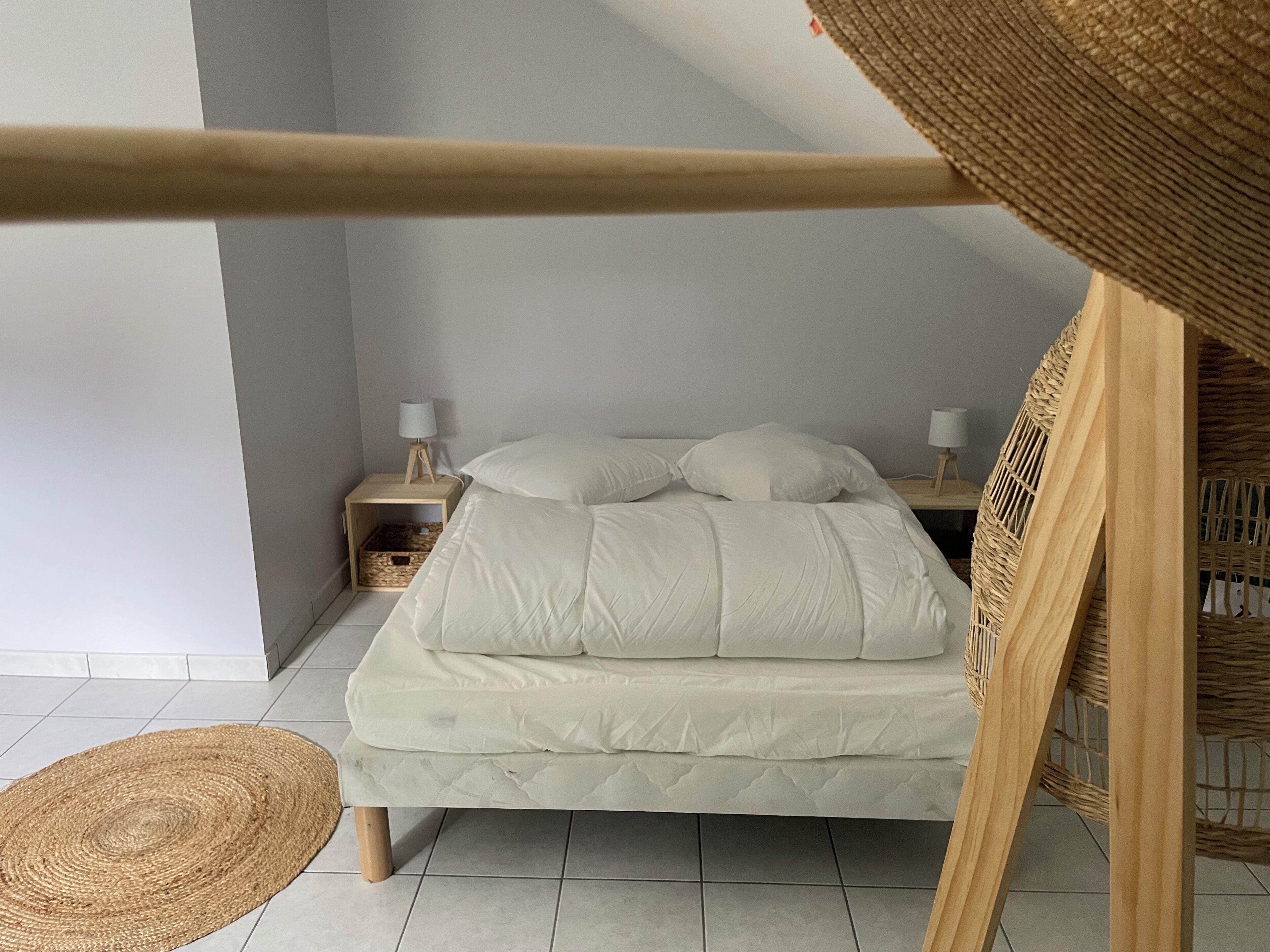A bedroom with a bed, two bedside tables with lamps, a woven chair, and a woven rug.