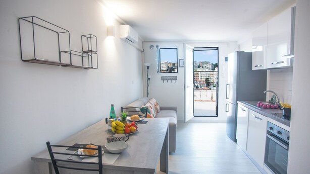 A modern kitchen with a dining area, a built-in oven, and a view of the city through the open door. - Sea View Historic Center (Sanremo)