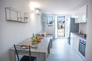 A modern kitchen with a dining area, a built-in oven, and a view of the city through the open door. - Sea View Historic Center (Sanremo)