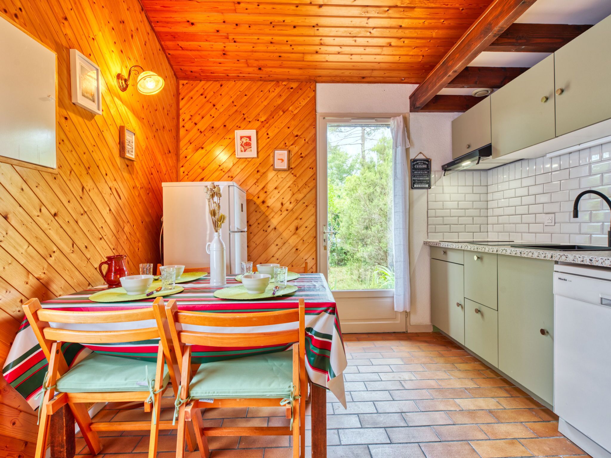 Ein Holzinnenraum mit einem für vier Personen gedeckten Esstisch, einem Kühlschrank und einer Küchenzeile mit weißen Schränken und einer gefliesten Spritzschutzwand.