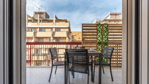 Ένα μπαλκόνι με ένα τραπέζι και καρέκλες, θέα σε κτίρια και ένα ξύλινο φράχτη.