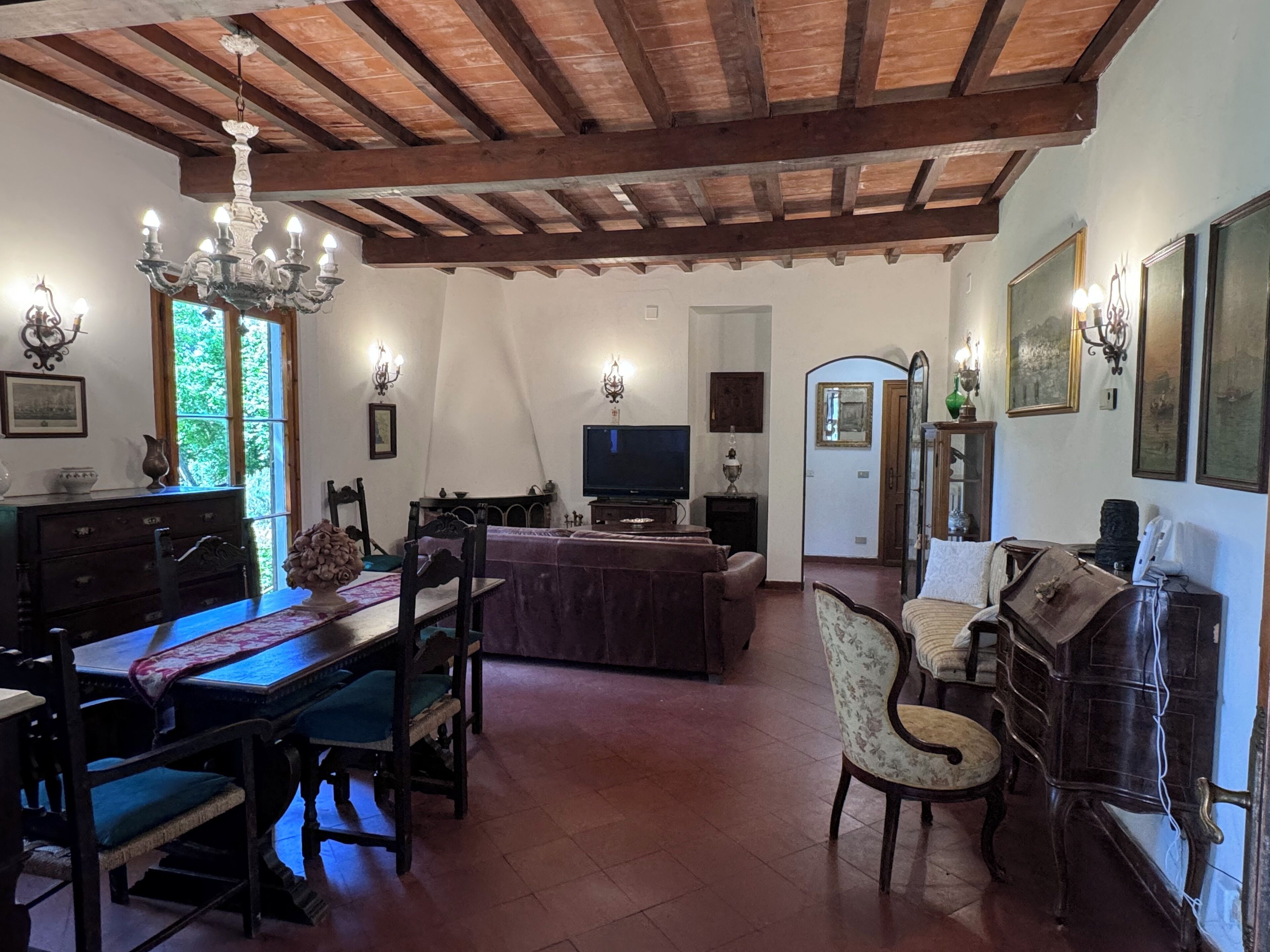 A traditional living room with a wooden ceiling, a dining area with a table and chairs, a sofa, and a television.