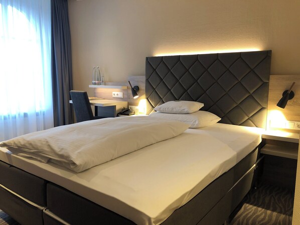 A hotel room with a large bed, a desk, and a chair.
