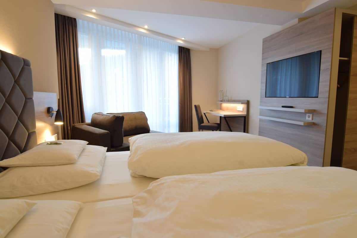 Habitación de hotel con dos camas, un escritorio, una silla, un televisor y una ventana con cortinas.