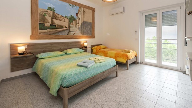 Una camera da letto con un letto grande, un letto più piccolo, un quadro appeso al muro, un comodino con una lampada e una finestra vista.