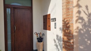 Una porta in legno con un pannello di vetro, un citofono montato a muro e un fioriera in pietra con ombrelli.