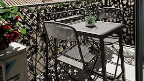 A balcony with a table and chairs, a decorative metal fence, and a view of the cityscape.