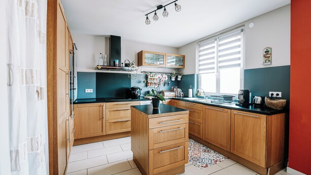 A kitchen with wooden cabinets, a black countertop, and a window with blinds.