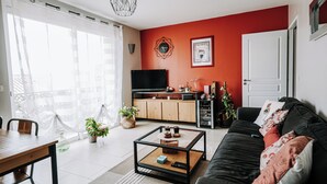 A modern living room with a black sofa, a coffee table, a TV, and a kitchen area with cabinets and a countertop.