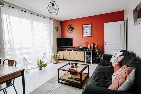 A modern living room with a black sofa, a coffee table, a TV, and a kitchen area with cabinets and a countertop.