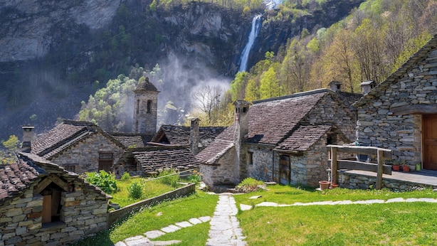 Un pueblo de piedra con arquitectura tradicional, un camino de piedra y una cascada al fondo.