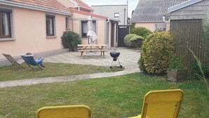 A residential backyard with a lawn, a barbecue grill, a picnic table, and two yellow chairs. - Gîte Chez Mamie 
A pleasant and quiet cottage by the sea (Saint-Marcouf)