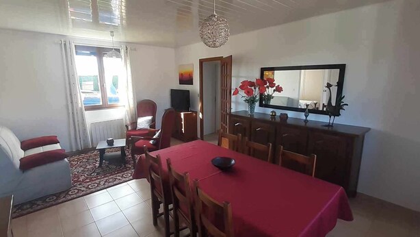A dining area with a red table and chairs, a wooden cabinet, and a mirror above the counter. - Gîte Chez Mamie 
A pleasant and quiet cottage by the sea (Saint-Marcouf)