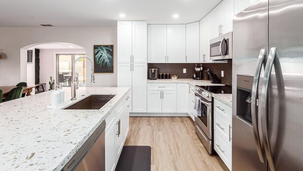 A modern kitchen with white cabinets, stainless steel appliances, and a marble countertop.
