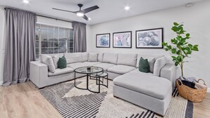 A modern living room with a sectional sofa, a coffee table, a ceiling fan, and framed artwork on the wall.