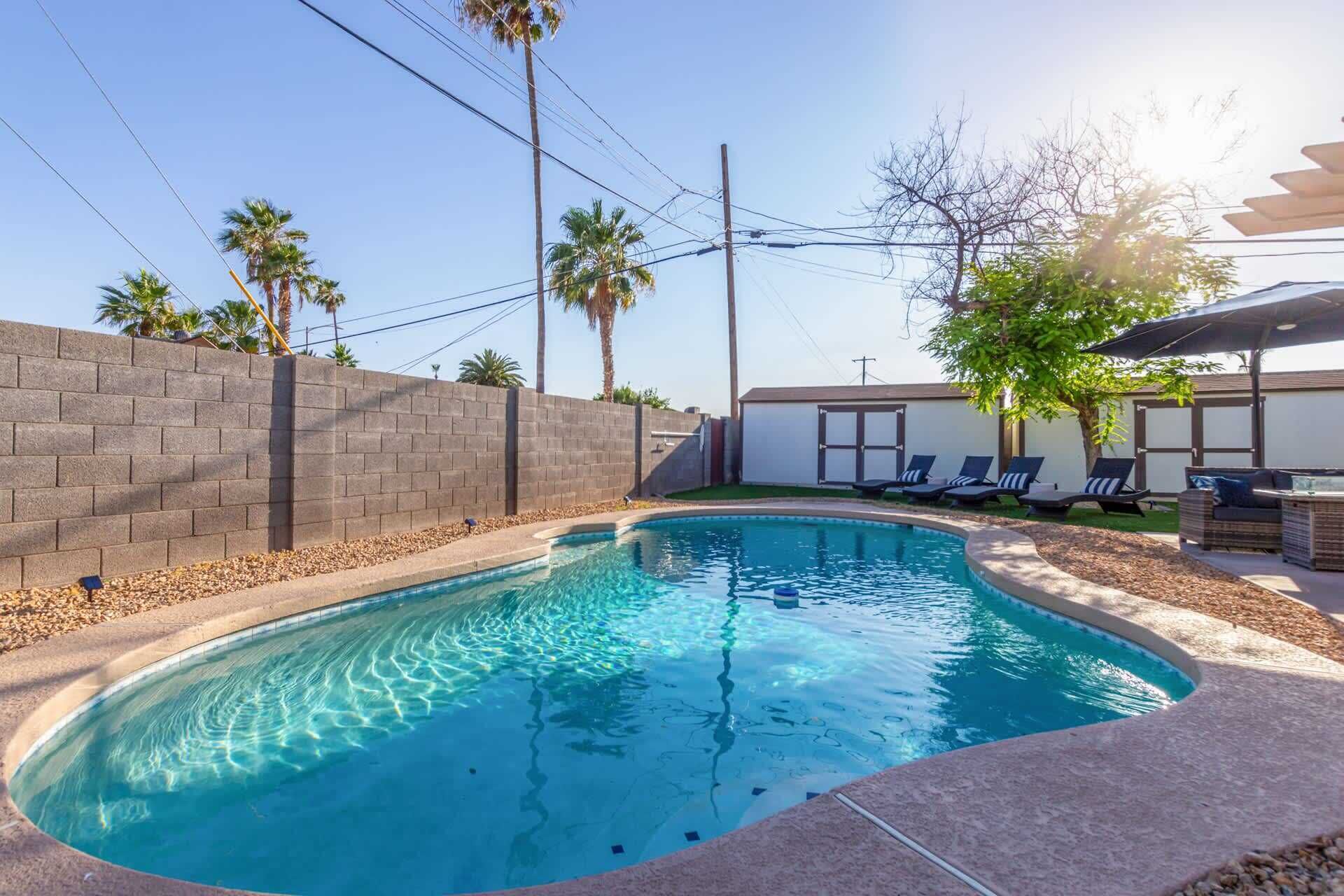 Una piscina con borde curvo, rodeada por un muro de ladrillo y una pequeña zona de terraza con sillas reclinables.