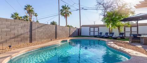 Una piscina con borde curvo, rodeada por un muro de ladrillo y una pequeña zona de terraza con sillas reclinables.