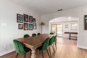 Un comedor con mesa de madera y sillas verdes, una pared decorada con cuadros y una puerta que da a un patio exterior.