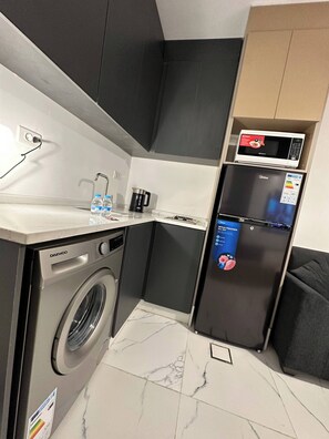 A compact kitchen with a washing machine, a microwave, and a refrigerator.