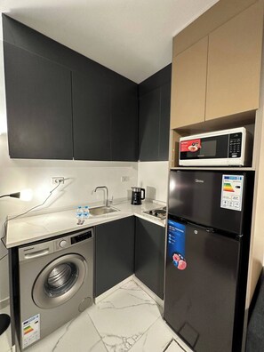 A compact kitchen with a washing machine, a microwave, and a refrigerator. - Stylish Luxe Apartment Fr 0003 (Amman)
