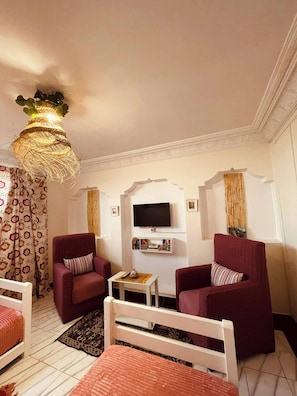 Un salón con dos sillones rojos, una mesa de centro blanca, un televisor montado en la pared y una lámpara colgante decorativa.