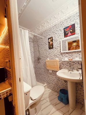 Un baño con inodoro blanco, lavabo, ducha con cortina y pared con azulejos decorados con un motivo floral.