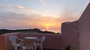 Un balcó amb cadires de plàstic blanc i una taula, amb vista a un capvespre i a les colines llunyanes.