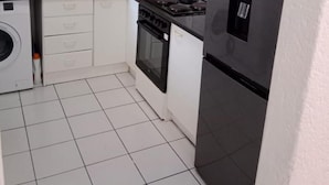 Una cocina compacta con armarios blancos, estufa negra, horno integrado, lavadora y refrigerador de acero inoxidable.