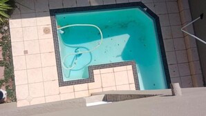Una piscina con borde de baldosas, una manguera y una escalera.