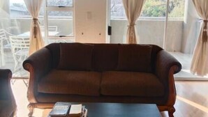 Una sala de estar con un sofá marrón, una mesa de centro negra y dos ventanas con cortinas.