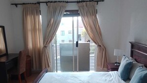 Habitación de hotel con cama, escritorio, silla, lámpara y vista al exterior.