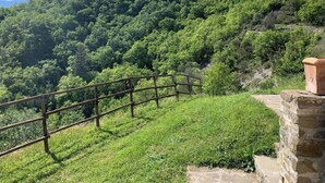 A stone structure with a metal railing on a grassy slope, overlooking a densely forested hill. - Apartment on the Hill Between Gubbio and Perugia (Perugia)