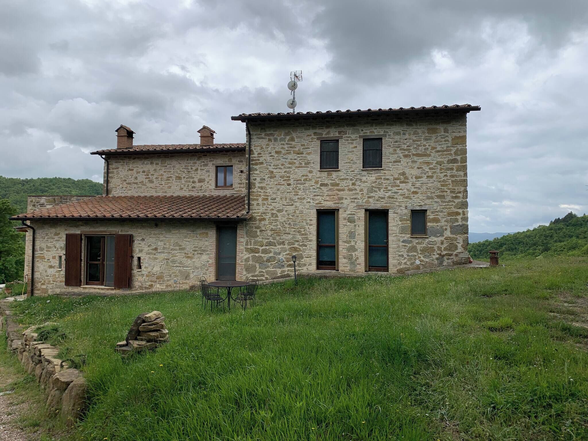 A stone house with a tiled roof, a small balcony, and a stone wall with a gate.