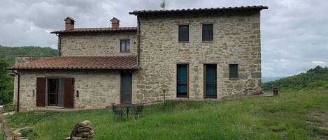 A stone house with a tiled roof, a small balcony, and a stone wall with a gate.