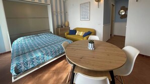 Pieni huone, jossa on sänky, pieni ruokapöytä ja keltainen sohva.