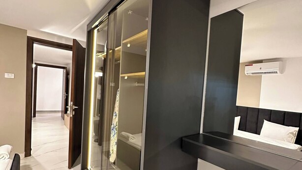 A modern hotel room with a large sliding glass door closet, a bed with a black headboard, and a bedside table. - Stylish Luxe Apartment Fr 0006 (Amman)