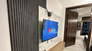 A modern interior with a flat-screen TV mounted on a marble wall, a wooden door, and a marble floor. - Stylish Luxe Apartment Fr 0006 (Amman)
