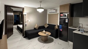 A modern living room with a sofa, coffee table, and a kitchen area with a refrigerator and microwave. - Stylish Luxe Apartment Fr 0006 (Amman)