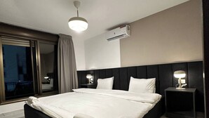 A hotel room with a large bed, two bedside tables with lamps, a ceiling light, and an air conditioning unit. - Stylish Luxe Apartment Fr 0006 (Amman)