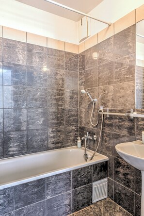 A modern bathroom with a bathtub, shower, and sink. - Central Capital Apartments (Budapest)