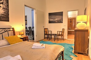 A hotel room with a bed, a desk, a chair, a wardrobe, a bathroom with a shower, and a door leading to another room. - Central Capital Apartments (Budapest)