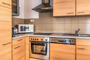 Eine Küche mit Holzausstattung, einer Edelstahl-Dunstabzugshaube, einer Mikrowelle, einem Geschirrspüler und einem Doppelbackofen.