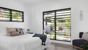 A bedroom with a bed, a chair, a window with blinds, and a view of greenery outside. - 4 Bedroom Luxury House in Port Douglas (Port Douglas)